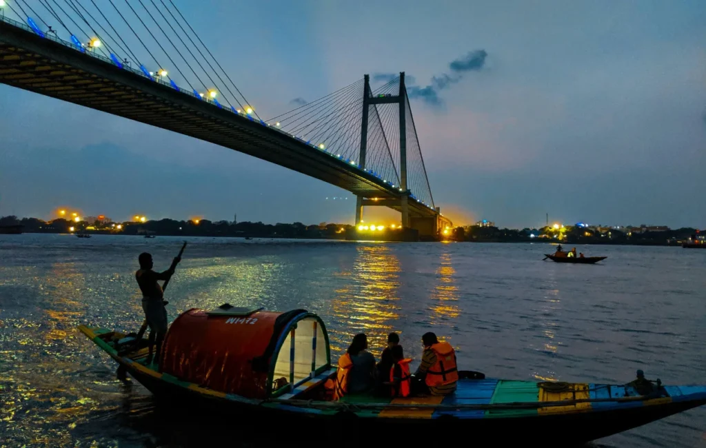 This image captures a sunset scene at the Hooghly River in Kolkata, India, featuring the Vidyasagar Setu (Second Hooghly Bridge). 